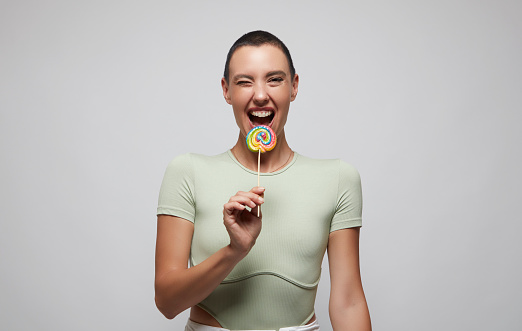 Studio portrait of a beautiful young woman sucking on a red lollipop against a green background
