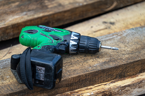 Green cordless screwdriver is lying on rough, damp boards on street. oncept of construction and garden exterior works.