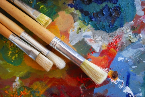 An art background showing a well used palette and different styles of paint brushes.