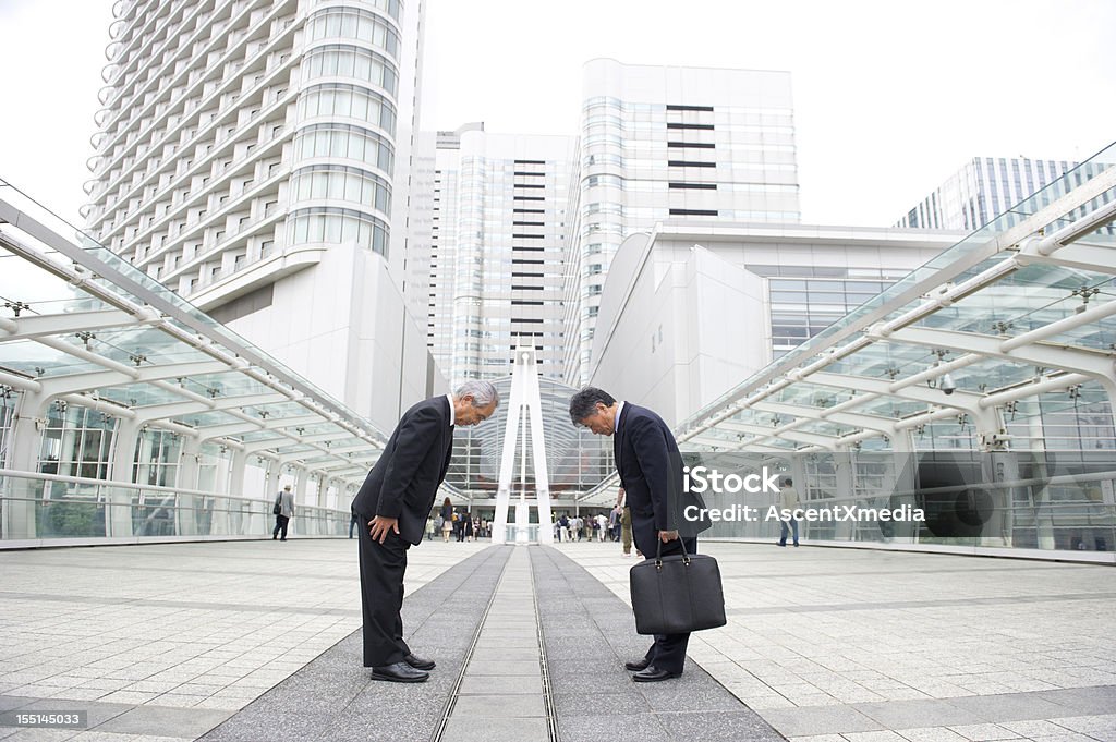 Two businessman bowing to each other on a pedestrian bridge Japanese Businessmen bowing Greeting Stock Photo