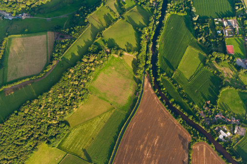 Vibrant green crops, ploughed fields and pasture, hedgerows and woodland surrounding farms and country homes beside an idyllic rural patchwork quilt landscape from high above. ProPhoto RGB profile for maximum color fidelity and gamut.