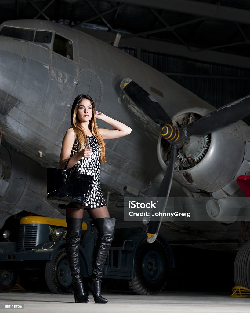 Travel Fashion Attractive young fashion model poses with bag by vintage aeroplane. Military Airplane Stock Photo