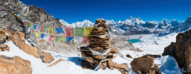 Colourful Buddhist prayer flags flying from a stone cairn overlooking the iconic summit pyramid of Mt. Everest (8848m) and the snow capped peaks of the Sagaramath National Park deep in the Himalaya mountains of Nepal under panoramic blue skies. ProPhoto RGB profile for maximum color fidelity and gamut.