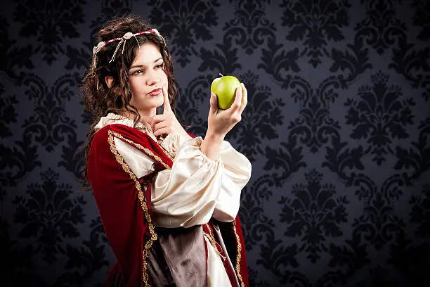 A beautiful young damsel dressed in period clothing holds a green apple and tries to decide whether to eat it or something less healthy.
