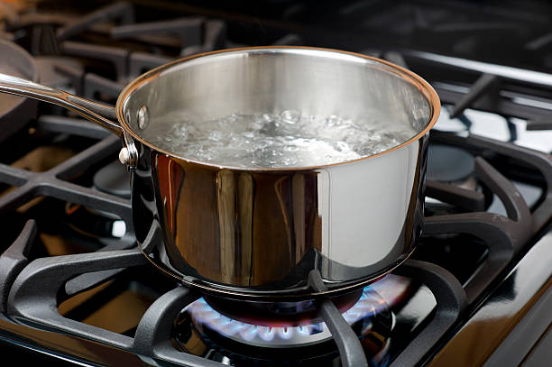 Water Boiling on a Gas Stove, stainless pot. Water bubbles and boils on a gas stove or range in a home kitchen.  Blue flame and stainless steel pot. burner stove top photos stock pictures, royalty-free photos & images