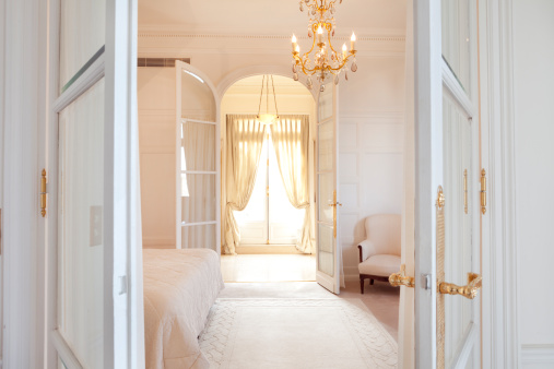 All white luxurious Parisian style bedroom suite with golden accents on the chandelier and door handles.  