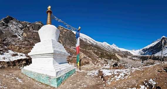 Traditional white-washed stupa and colourful Buddhist prayer flags under blue panoramic Himalayan skies at the Sherpa village of Thame, deep in the Everest National Park of Nepal. ProPhoto RGB profile for maximum color fidelity and gamut.