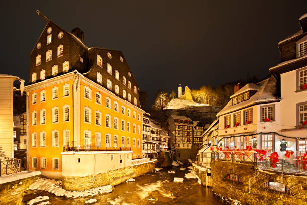 The Rur at the Red House (Rotes Haus) in the German Eifel village of Monschau during christmas time at night, the old castle ruin in the background.