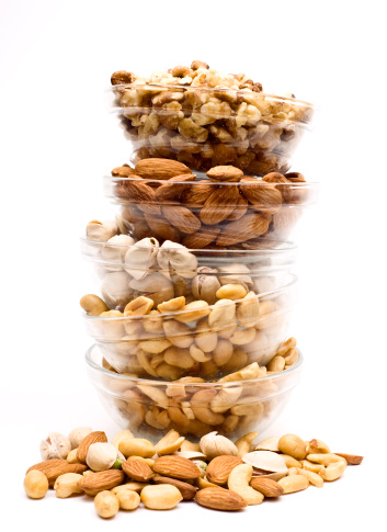 Five different varieties of nuts (cashew, pea nuts, pistachio, almond, walnut) stacked in a bowl isolated on white background
