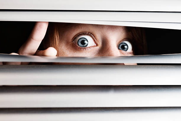 istock Wide eyed girl peeps through venetian blinds 155147575