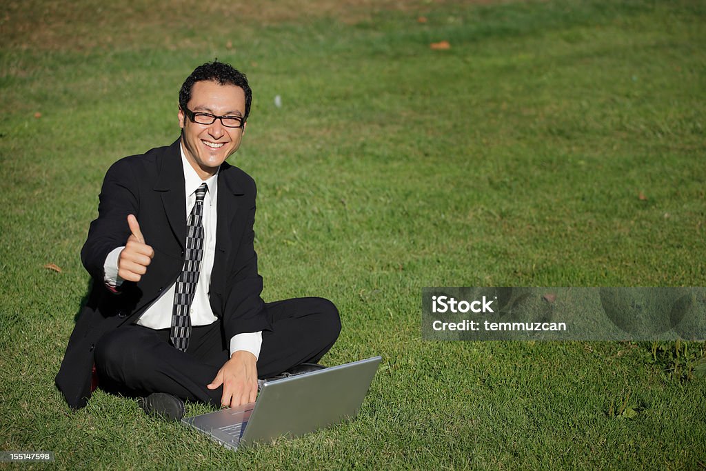 Homme d'affaires donnant un "pouce levé" dans l'herbe à l'aide d'un ordinateur portable. - Photo de Adulte libre de droits