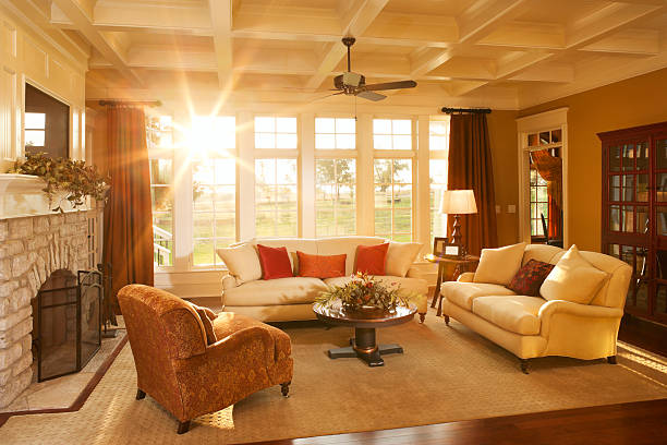Well-appointed traditional living room with beamed ceiling Warm afternoon sunlight pours into an elegant home's living room with a stone fireplace and large windows looking out into the yard. electric fan photos stock pictures, royalty-free photos & images