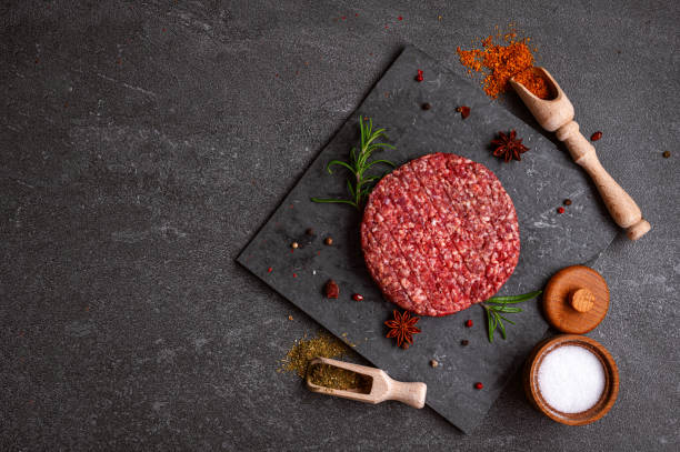 istock Juicy raw burger patty against a dark backdrop. 1551480290