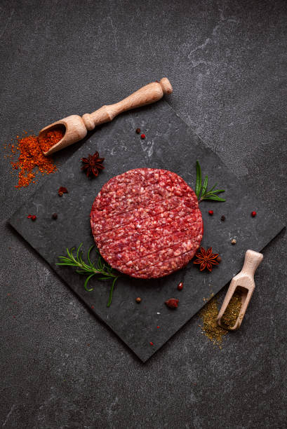 istock Juicy raw burger patty against a dark backdrop. 1551480525