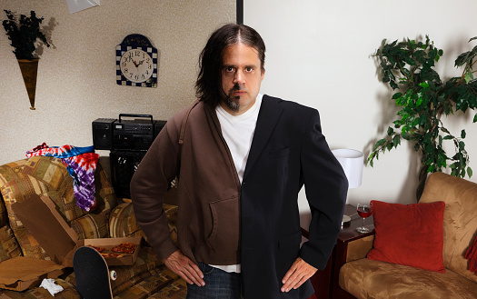 A man standing in a room. On one side he has long messy hair and clothes, and on the other side he has styled hair and nice clothes.  Half of the room is extremely messy and poorly decorated, while the other half is clean and neat.