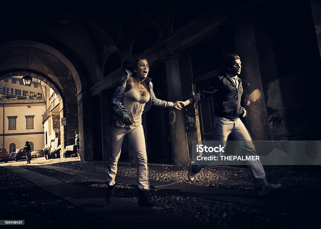 couple running scare couple running thru an ominous street tunnel in small town of northern italy as someone bad was chasing them. Running Stock Photo