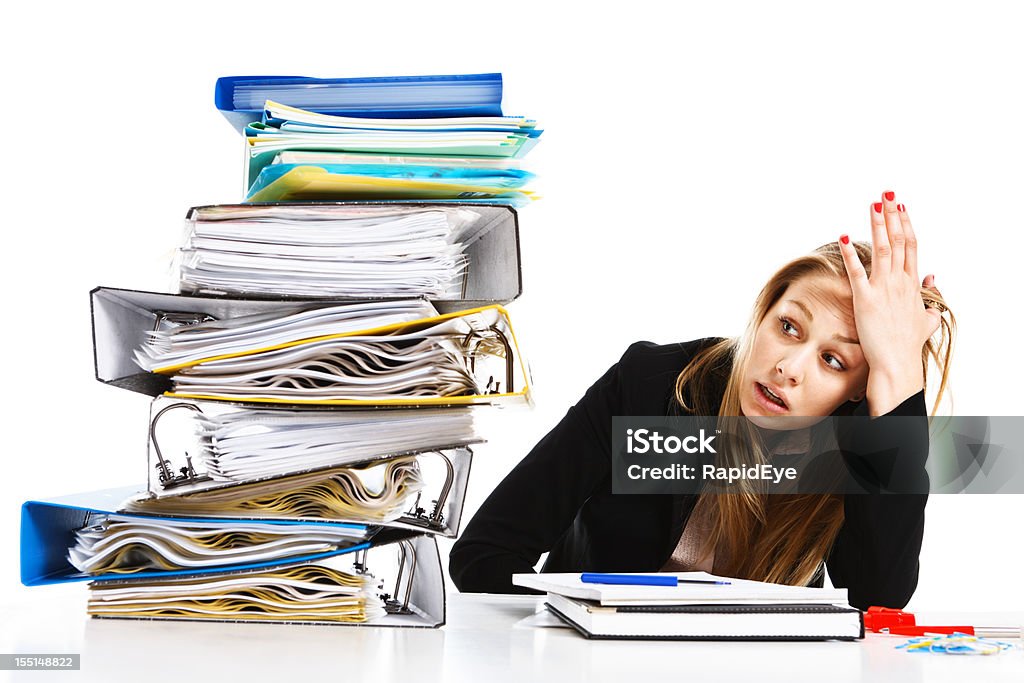 Impossible amount of work overhelms unhappy young businesswoman This attractive young businesswoman, her head in her hands, looks sideways in despair at the overwhelmingly huge pile of work files beside her.  Office Stock Photo