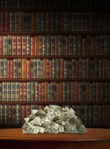 One Hundred Bills Piled on Table with Books in Background.