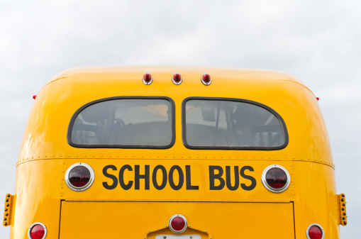 Rear view of an antique yellow school bus isolated on an overcast day.