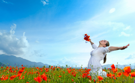 woman with arms raised in poppy field relaxing.