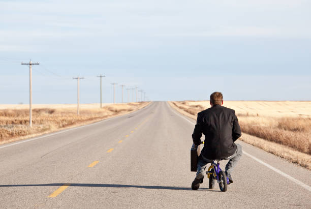 Businessman Commuting on Tiny Bicycle A humorous concept image of a businessman commuting to work on a tiny bicycle. Business concept. Efficiency. funny. challenge, adversity. green. environmental issues. effort. intelligence. direction. determination. on the move. the way forward. irony stock pictures, royalty-free photos & images