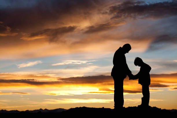 Silhouette of Father and Son Praying A silhouette of a father and son praying. Themes include parenting, father, love, Christianity, bonding, love, sharing, moment, special, evening, outside, rural, religious, teaching, mentor, care, holding hands, togetherness, dad, son, child, family, single father, gratitude, attitude, caring, responding, hope, health, mental health, wellness, lifestyle, commitment, faith, dedication, and salvation. silhouette of bad boy stock pictures, royalty-free photos & images