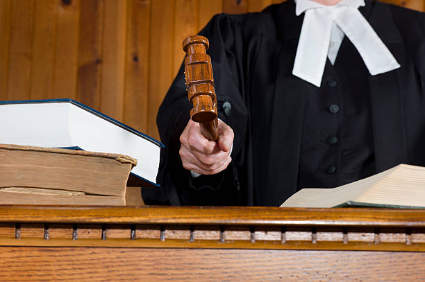 A judge hits the desk or bench with a Gavel during a trial.  Robes are traditional British Commonwealth Barrister gowns.  Courtroom background with copy space.