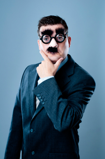 Funny looking business person is looking at the camera. He is disguised by a plastic nose, fake mustache and eyebrows. He is also wearing glasses. Looks like he is thinking about something.