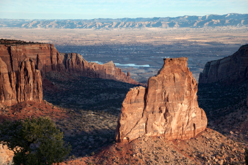 Early morning sunlight hits the cliffs and spires in Grand Junction's Colorado National Monument. The Colorado river flows in the background.
