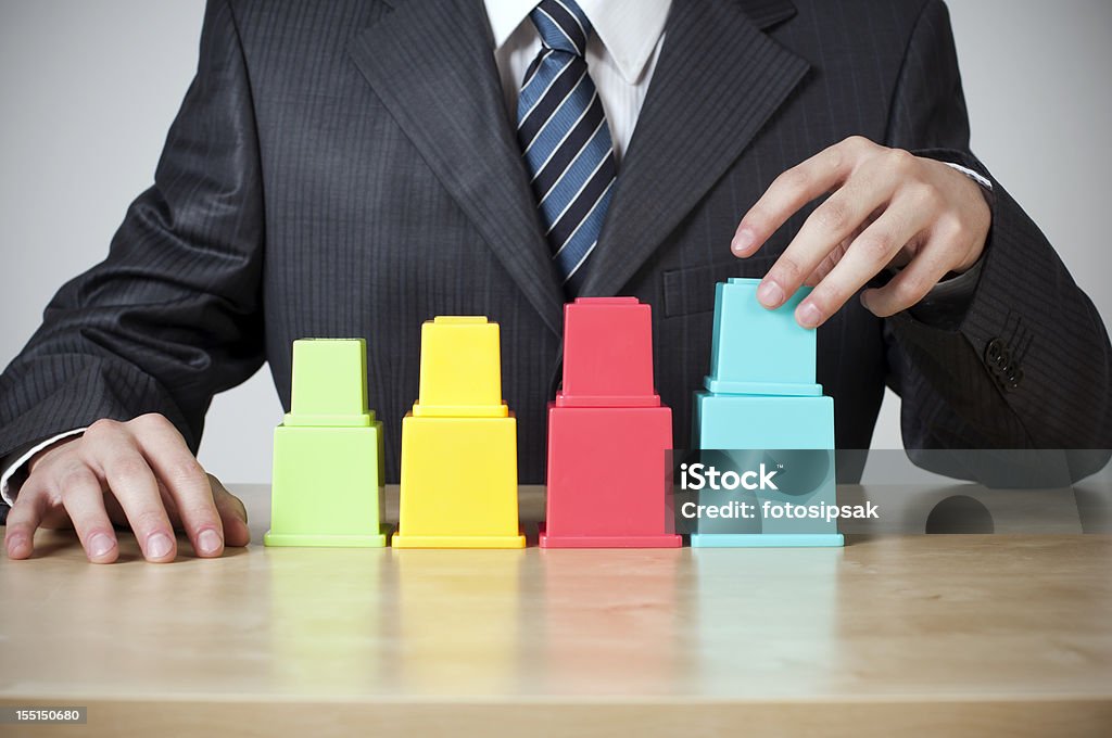 graph businessman making a rising bar graph with multicolored cube block toys on the table Moving Up Stock Photo