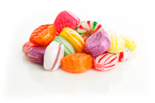 Traditional hard sugar candies on a reflective surface isolated on a white background. Focus is on the front of the pile of candies.