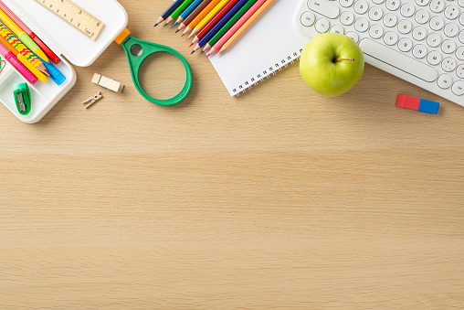 Embrace the modern approach to education with this top-down photograph, featuring a keyboard, notepad, pencil box and various school supplies backdrop. Ample copy-space for text or advertising