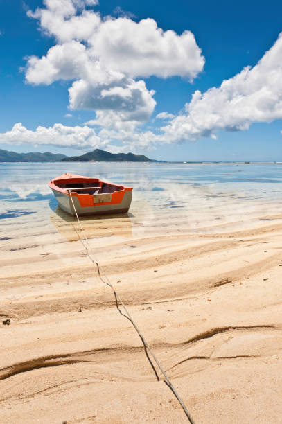 Small boat moored on a sandy beach in the clear turquoise waters of an idyllic tropical lagoon under deep blue Indian Ocean skies, La Digue, Seychelles. ProPhoto RGB profile for maximum color fidelity and gamut.
