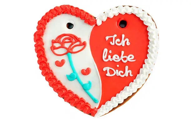 gingerbread heart cookie with German words "Ich liebe dich" (engl. I love you) in red and white. On left side a rose of icing. Typical Beer Fest or Valentines day gift on white background.