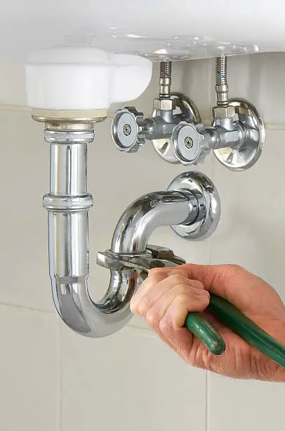 Photo of Hand of a plumber fixing a sink with green tool