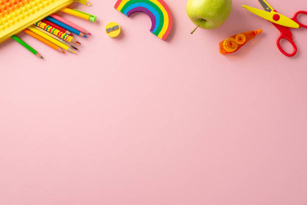 初等教育ツール。鮮やかなアイテムを紹介するトップビュー:色鉛筆、修正テープ、はさみ、シャープナー、リンゴでペンシルポーチをポップします。パステルピンクの背景。テキストや広告