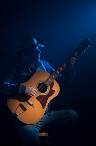 Country-Western guitar player against a dark background with spot light on the guitar. Blue accent light simulates stage appearance.