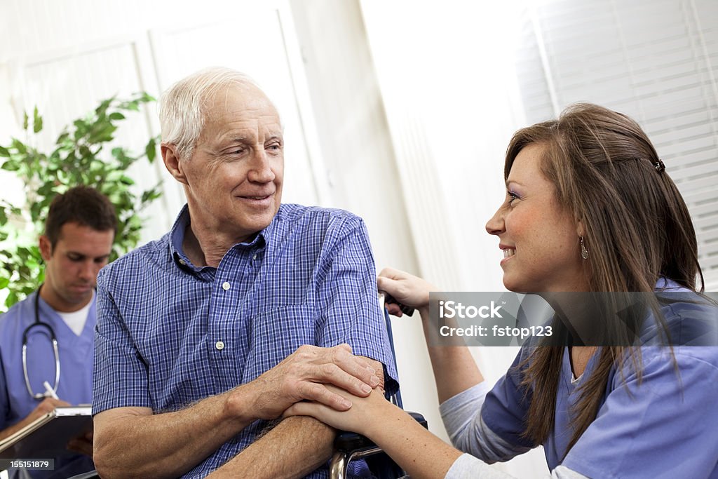 Physical therapist or nurse consoling senior man patient. Wheelchair. Doctor. Physical therapist or nurse consoling patient. Doctor in background. Face To Face Stock Photo