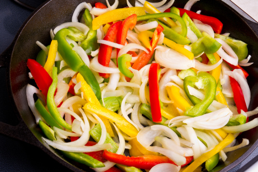 Sliced green, red and yellow bell peppers in a pan being sautéed in olive oil and spices
