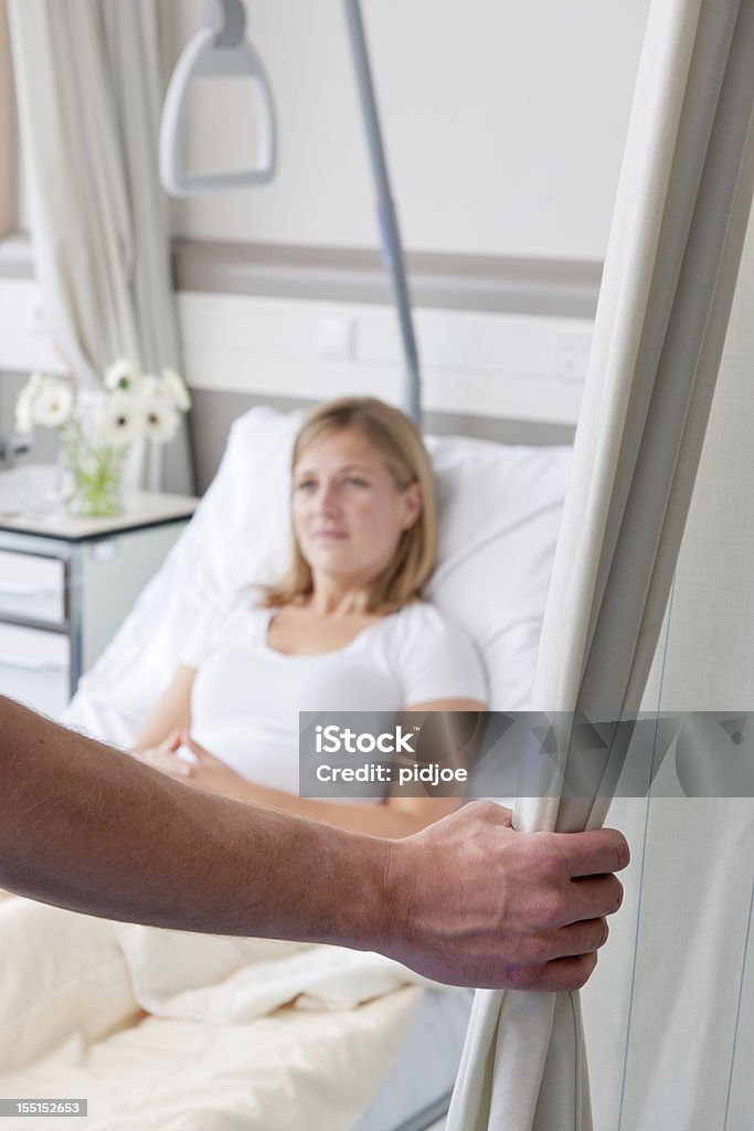 closing curtain around patient in hospital bed male nurse closing curtain around blond woman lying in hospital bed, focus on the foreground Privacy Stock Photo