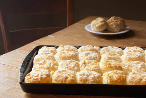 A well seasoned pan of hot, fresh biscuits (a southern staple) sitting on a pine harvest table bathed in warm sunlight.