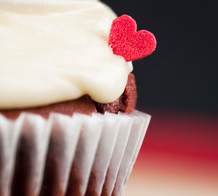 Macro image showing a small red love heart made of sugar, placed in the icing of a cupcake.
