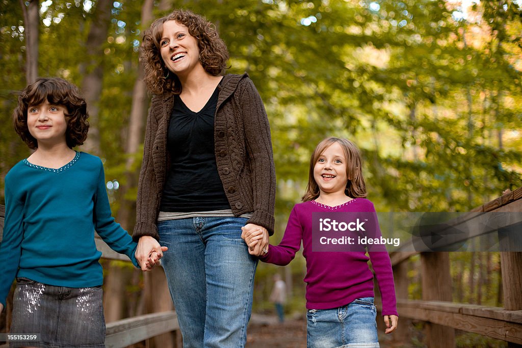 Sorridente madre e figlie a piedi il ponte di legno all'aperto - Foto stock royalty-free di 30-34 anni