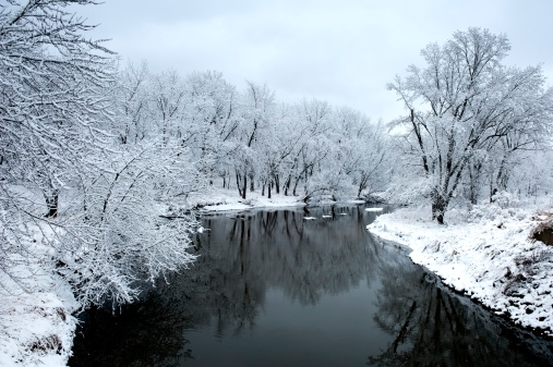 A beautiful winter landscape with an icey cold river, and fresh snow on the trees.