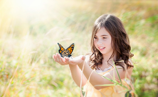 Young girl in a field holding a monarch butterfly.