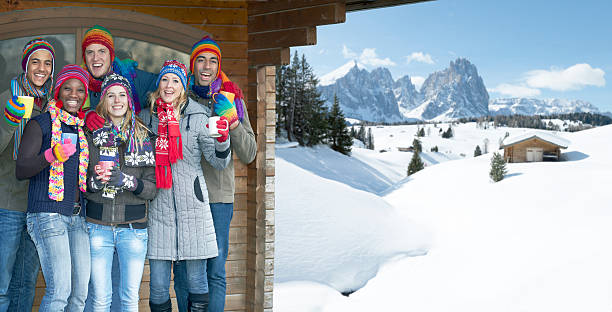 Young multi-ethnic group celebrating under cabin roof in snowy mountains Three young multi ethnic couples in multi colored winter clothes celebrating vacations with mulled wine under roof of cabin in snowy mountain area. Langkofel mountain (Dolomites, Alto Adige, Italy) in the background. Shallow DOF with selective focus on the women. apres ski party winter cabin stock pictures, royalty-free photos & images