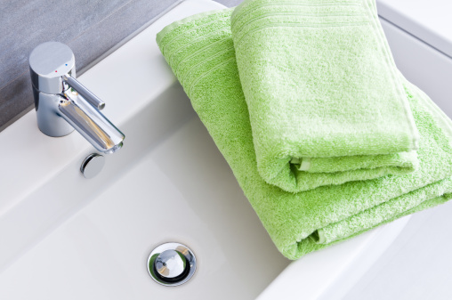 Bathroom sink with two clean green towels in different sizes.