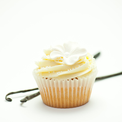 Close-up photo of a vanilla cupcake on white background with two vanilla beans next to it.