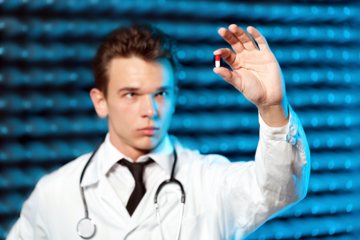 Young pharmacist holding medicine pill. Shallow DOF, focus on capsule.