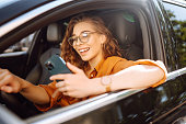 Happy woman in the car in the driver's seat looks at the smartphone.  Business, technology concept.